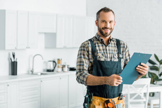 Plumber smiling with a clipboard in a customer kitchen